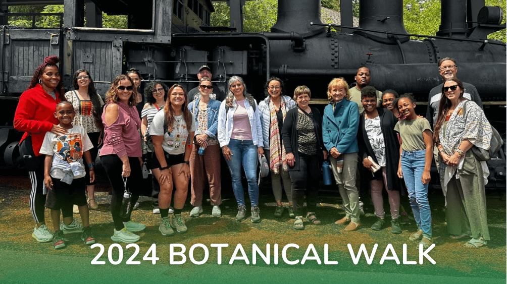 A group poses in front of a large black train engine before going on the botanical walk