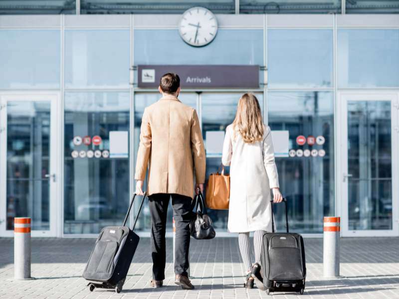 Two people walking into the airport with rolling suitcases