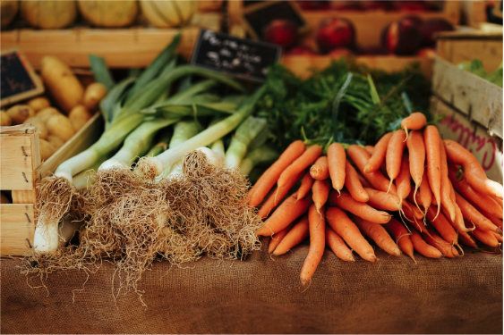 Organized piles of potatoes, leeks, and bundles of carrots rest on a rustic farmers market table