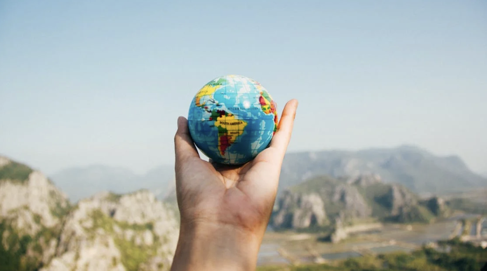 A person holds a vibrant globe up against a mountainous landscape.